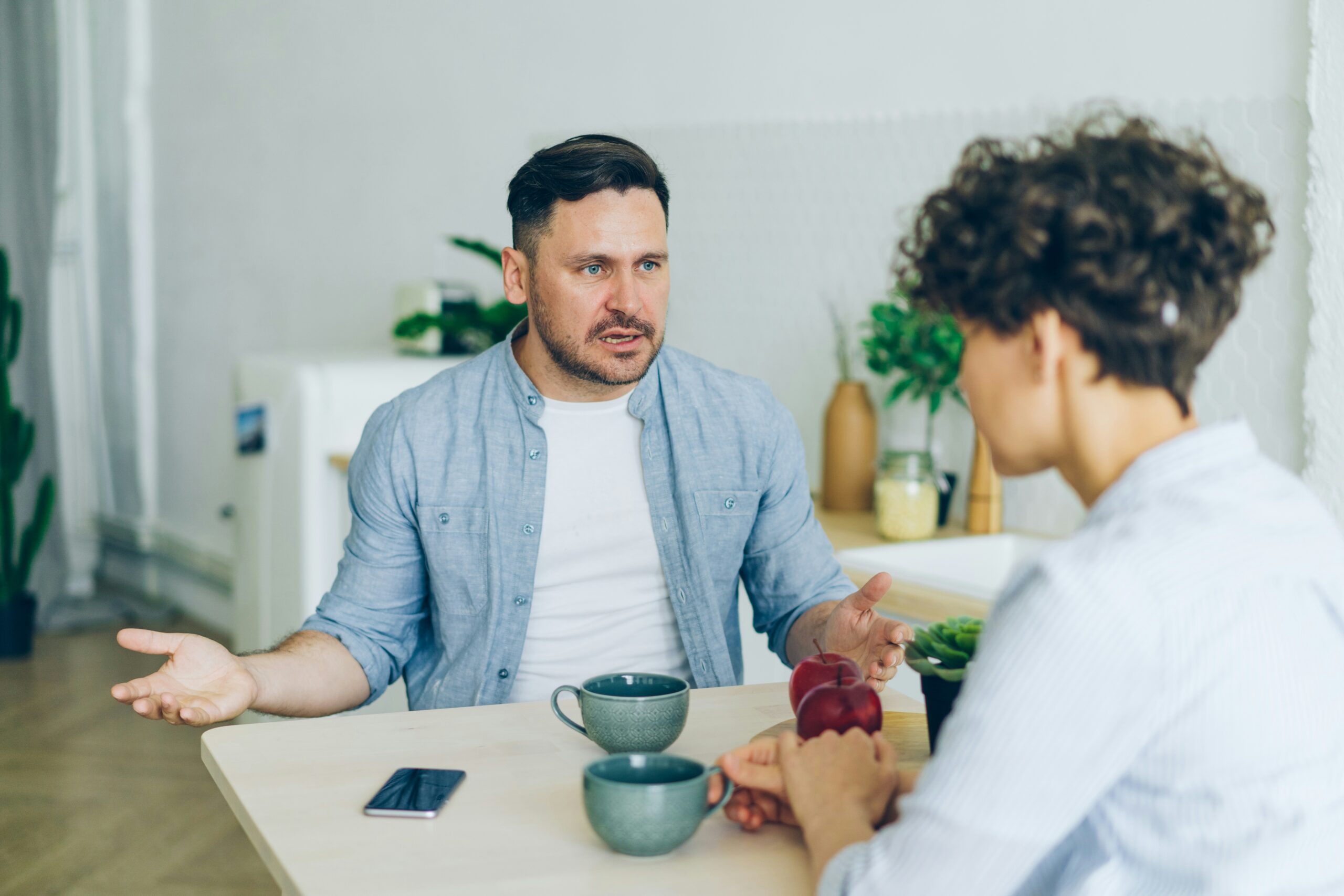 Couple in a tense conversation at the kitchen table, representing the strain of the mental load in marriage and the need for relationship counselling support