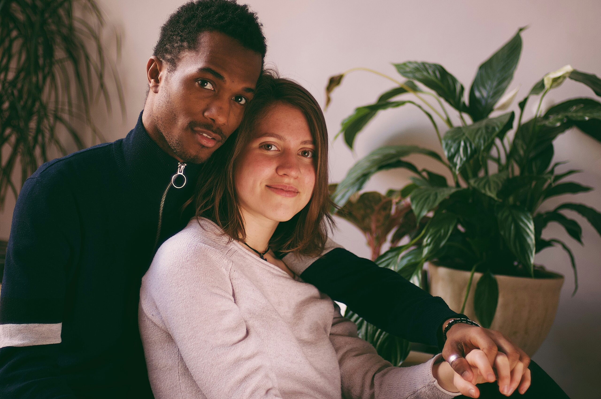 Affectionate interracial couple sitting close together and holding hands, symbolising love, unity, and the themes of intercultural and interracial relationships.