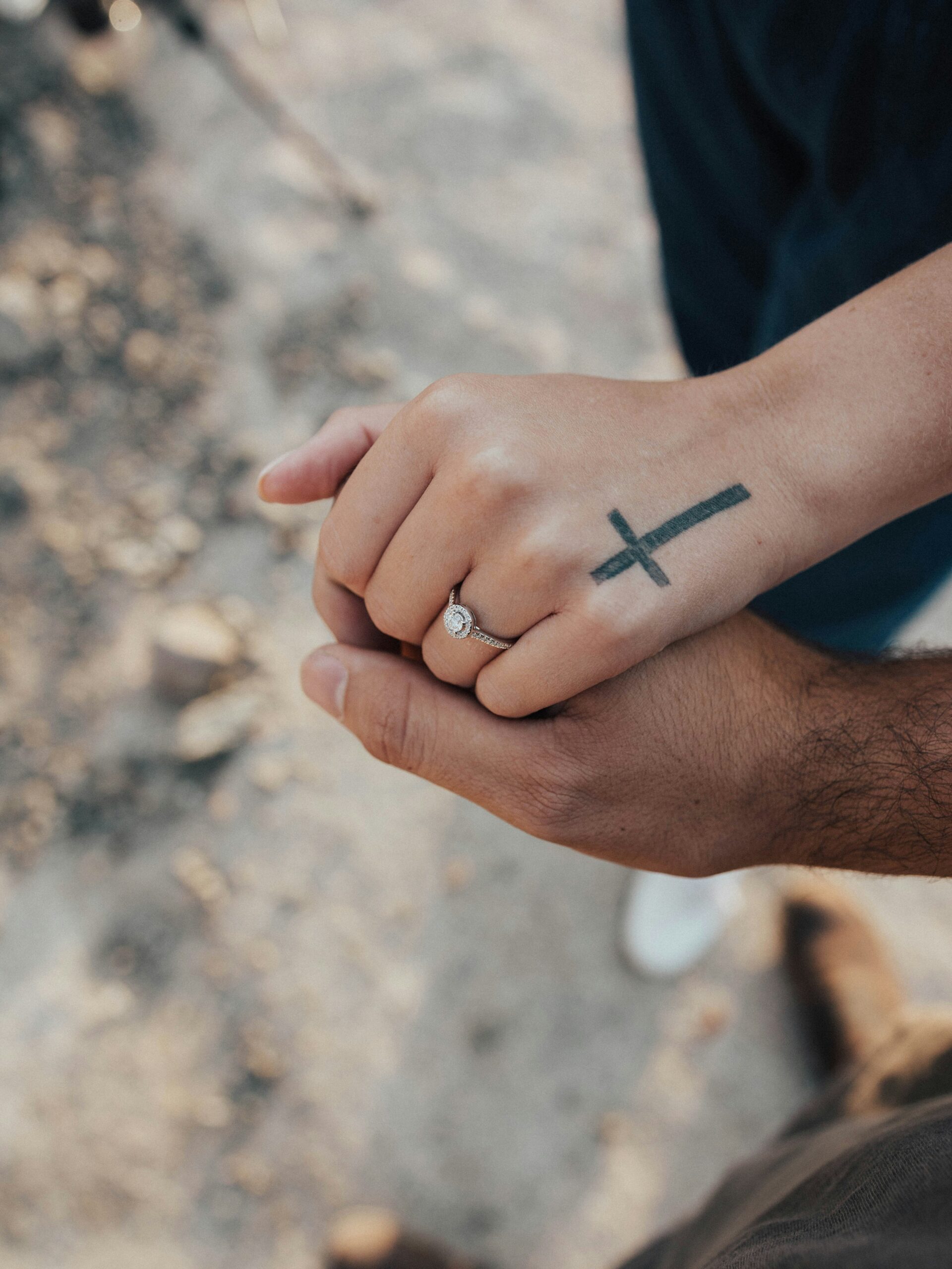 Christian couple holding hands with a cross tattoo and engagement ring, representing faith, marriage, and the decision to seek couple therapy for healing and growth